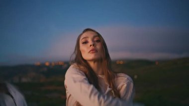 Akşam doğa portresinde kucağında hafif bir bez tutan seksi kadın. Baştan çıkarıcı esmer model kamera poz veriyor beyaz kanat çırpan kumaşlarla el sıkışıyor. Ciddi kız dik dik bakıyor.