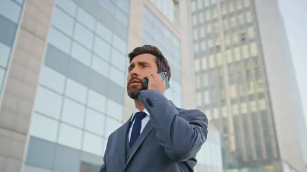 Company worker talking mobile phone walking urban business district close up. Elegant bearded boss calling partner going on office work. Serious manager discussing cooperation by phone call outdoors.