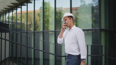 Ciddi bir ustabaşı telsizle konuşuyor. İş bölgesini kapatıyoruz. Kasketli, el bilgisayarlı telsizle konuşan, gülümsemeyen bir adam şehir merkezinde yürüyor. Kendine güvenen inşaatçı işçilere talimat veriyor