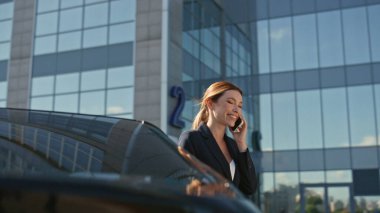 Sunny caddesinde pahalı bir arabaya yaslanıp cep telefonuyla konuşan şık bir yönetici. Gülümseyen kadın CEO ofis binasının yakınındaki akıllı telefonu arıyor. Mutlu iş kadını dışarıda dostça sohbet eder.