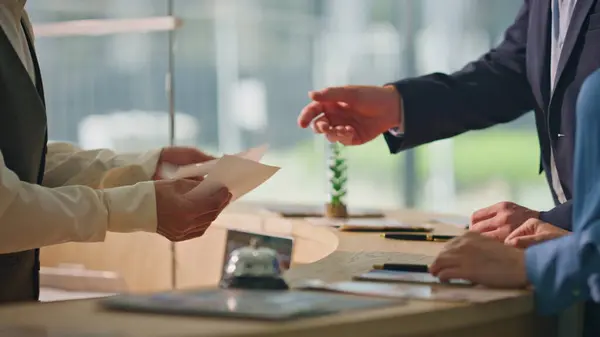 Receptionist hands giving keys at hotel counter closeup. Tourist couple check in arriving accommodation. Unrecognized professional concierge work help smiling clients in lobby. Business trip service.