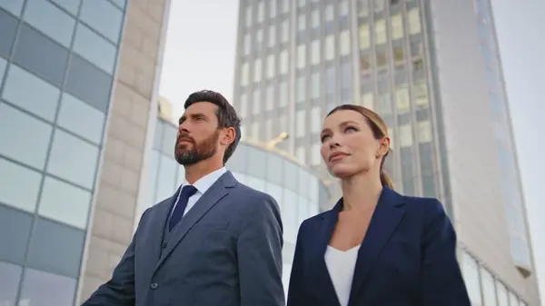 Successful business people walking urban centre in elegant suits close up. Attractive businesswoman going on work with confident businessman. Two company partners hurrying on business meeting together
