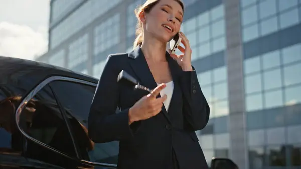 Successful car saleswoman calling on street playing with keys in hand closeup zoom out. Happy businesswoman talking smartphone leaning on premium auto. Elegant lady automobile buyer speaking cellphone