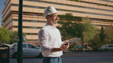 Odaklanmış mühendis güneş ışınları şehrinde bina planlarını kontrol ediyor. Bronzlaşmış bir adam, elinde planlarla Summer Caddesi 'nde telsiz kullanıyor. Ciddi bir inşaatçı dışarıda çalışma talimatı veriyor.