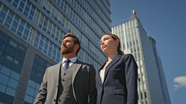 Güneşli kentlerde resmi takım elbiseli iki iş ortağı poz veriyor. Uzaklaş. Mesafeye bakan kendine güvenen takım arkadaşları lüks otomobillerin yanında duruyorlar. Başarılı ortaklık kavramı.