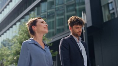 İşletme müdürleri birlikte dışarı çıkıyorlar. Yakın çekim. Güler yüzlü ortaklar işten sonra güneşli şehir merkezinde yürüyorlar. Şık iş arkadaşları şehir caddesi projesini tartışıyor. Kurumsal insan kavramı