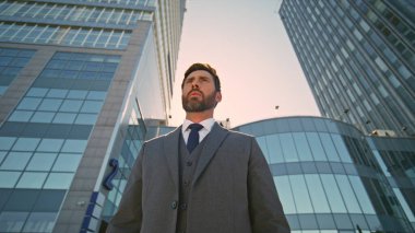 Yaz güneşinde caddede duran yakışıklı patron. Sakallı zengin işadamı, uzaklardan modern ofis binasının önünde poz veriyor. Açık havada şık takım elbiseli, kendinden emin, orta yaşlı bir adam..