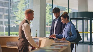 Modern lobide kredi kartıyla ödeme yapan bir kadın. Gülümseyen misafirler vardıktan sonra yerleşmeye başlıyorlar. Profesyonel dost canlısı kapıcı masada müşterilerle konuşuyor. Müşteri hizmetleri kavramı