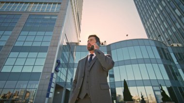 Şehir güneşinde cep telefonuyla konuşan zeki adam yakınlaş. Kendine güvenen zengin yönetmen iş yerinden akıllı telefonu arıyor ofis binasının dışında mola veriyor. Ciddi patron şirket işlerini telefonla konuşuyor..