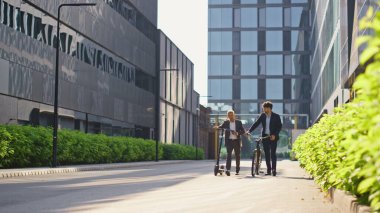 Şirket çalışanları işten sonra bölge yürüyüşü yapıyor. Çevre dostu ulaşım. İki neşeli adam, ellerinde elektrikli scooter ile şehir merkezine gidiyorlar. Ofis arkadaşları iş görüşmelerini takım elbiselerle yapıyorlar..