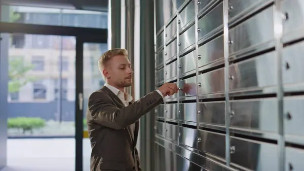 Man open private mailbox checking correspondence in corridor closeup. Upset guy looking letter feeling disappointed in hall. Successful sad businessman in suit entering building holding mail envelopes