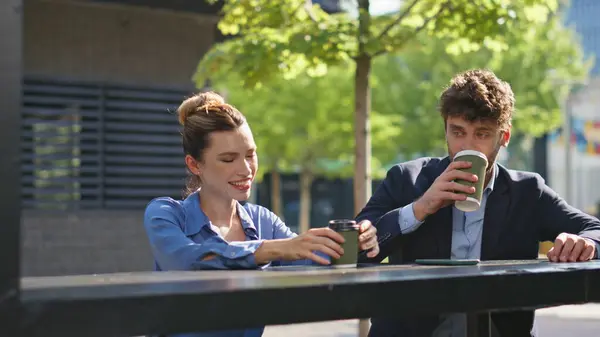 Two workers drinking coffee on street closeup. Cheerful business people talking flirting outdoors. Happy smiling partners enjoying beverage laughing in city park together. Work friendship concept