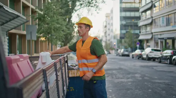 Uniform worker cleaning city. Hardhat urban cleaner in vest throw away rubbish preparing to construction site works. Municipal latina guy working alone at morning town. Environment service concept