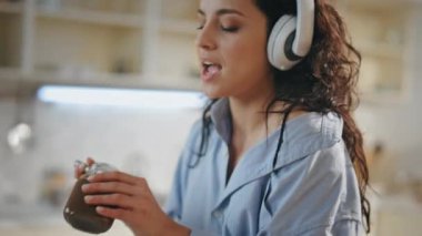 Mutfakta modern kablosuz kulaklıkla müzik dinleyen bir kadın. Çekici genç kız bıçaktan çikolata ezmesi tadıyor. Tasasız, rahat ev hanımı kulaklıkla yemek hazırlıyor.