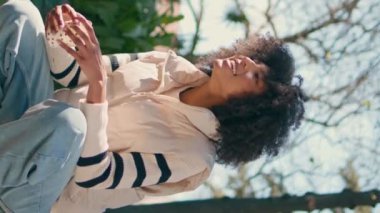 Anne kızı yeşil parkta dinleniyor. Mutlu Afrikalı Amerikalı kadın, küçük tatlı bir kızın yanında çömelmiş güneşli bir hafta sonunun tadını çıkarıyor. Gülümseyen anne dikey olarak sevimli çocukla konuşuyor..