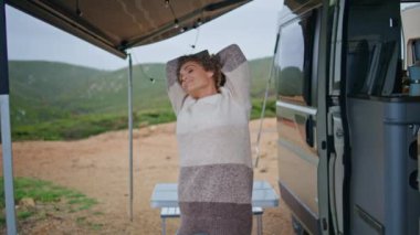 Sonbahar tatilinde karavanda vücudu geren kaygısız turistler. Kapatın. Gülen mutlu kadın teras karavanında duruyor bulutlu ve güzel doğanın tadını çıkarıyor. Minibüste özgürlük hisseden çekici kadın..