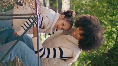 Kızını taşıyan bir kadın çitin üzerinden naklediyormuş. Neşeli Afro-Amerikan annesi küçük kızı alıp güneşli parkta dikey bir şekilde gezdiriyor. Mutlu anne çocukla doğada iyi eğlenceler..