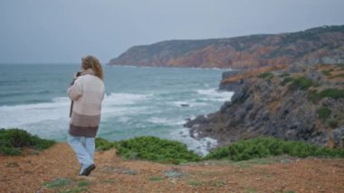 Soğuk bir günde okyanusta gezen rahat bir turist. Arkaya bakan kıvırcık saçlı kadın fırtınalı deniz dalgalarına bakıyor. Kıvırcık kadın kasvetli deniz tatilinde deniz manzarasının tadını çıkarıyor..
