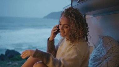Fırtınalı okyanus manzarasının tadını çıkaran bir kadın akşam kampı minibüsünü arıyor. Kıvırcık kadın turist deniz kıyısında karavanda oturan akıllı telefonlardan konuşuyor. Rahat bayanın karavanda cep telefonu bağlantısı var..