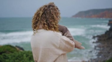 Mutlu bayan bulutlu haftasonunda deniz manzarasının keyfini çıkar. Gülümseyen orta yaşlı kadın sahilde dönüyor tatilde özgürlük huzurunu hissediyor. Kaygısız kadın tatilci kıyıda durup okyanus dalgalarını seyrediyor.