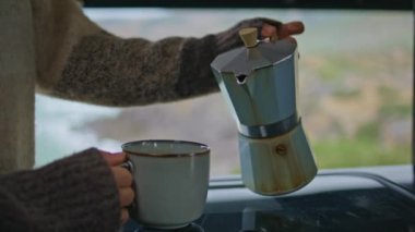 Kadın elleri bardağa espresso dolduruyor. Sabahın tadını çıkarıyor. Kapalı mekanda. Karavandaki kahve makinesinden bardağı dolduran tanınmayan bir kadın. Bilinmeyen kız deniz kıyısında rahatlatıcı aromatik bir içecek hazırlıyor.