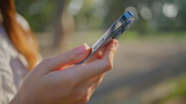 公園でデジタル通信を強調するスマートフォンを保持するクローズアップハンド 女性大人のタッチスクリーン携帯とのやり取り モバイルデバイス上の屋外ブラウジングは 現代的なデジタルライフスタイルを明らかに — ストック動画