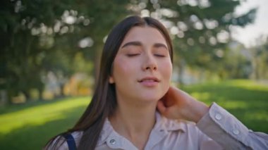 Mutlu kadın güneşli yeşil bahçe portresi üzerinde huzur içinde dinleniyor. Yakından sakin bir yüz hafif güneş ışığıyla yıkanmış. Kadın mutluluğu, doğal güzellikle harmanlanmış rahat park arka planında..