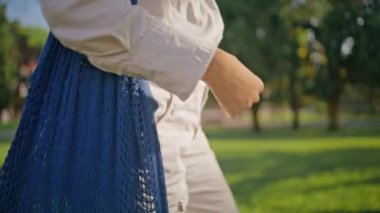 Sürdürülebilir çanta taşıyan rahat bir kadın güneşli doğada geziniyor çevre dostu yaşam tarzını destekliyor. Organik ürün alıcısıyla günlük park yürüyüşü. Bilinmeyen kız çevreye duyarlı boş zamanların tadını çıkarıyor.