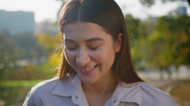 Mutlu kadın yakından gülümseyen, altın güneş ışığıyla yıkanmış bir portre. Huzurlu, rahat kız Green Park 'ta kaygısızca eğleniyor. Güneşli bahçede poz veren güzel bir model..