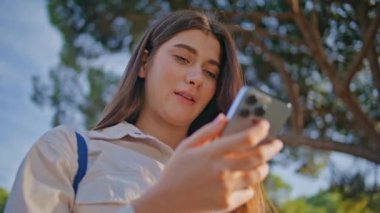 Ciddi bir kız cep telefonundan güzel, güneşli bir mekanda mesaj okuyor. Hafta sonu parkta yürürken akıllı telefon ekranına bakan çekici genç bir kadın. Odaklanmış esmer açık havada cep telefonu mesajları alıyor.