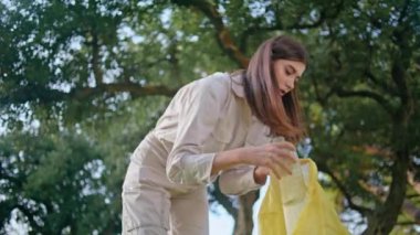 Parktaki çöpleri temizlemeye gönüllü biri. Elinde sarı bir çanta var. Çevreci kadın yeşil bahçede plastik çöp topluyor ve doğa kirliliğinden endişe ediyor. Çevresel koruma ile meşgul kadın çevreci aktivist.