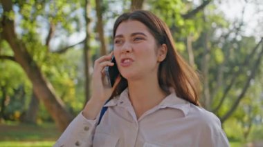 Sinirli bir kadın cep telefonundan konuşuyor. Sinirli görünüyor. Yeşil Park 'a yakın. Genç bayan yaz yürüyüşünde telefonla konuşmaktan hoşlanmadı. Genç kız ifadesi konuşmada rahatsız edici..