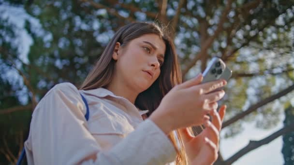 公園のクローズアップを探索する携帯電話を見つめる燃える少女 静かな夏の設定で スマートフォンで仕事のメールを読んでいる若い女性の肖像画 自然に関するテクノロジーとの関わり — ストック動画