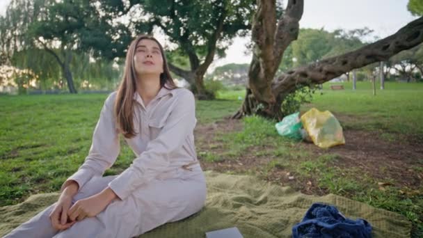 女人喜欢安静地坐在草地上晒太阳 年轻的微笑女士在野餐毛毯上放松一下 环保人士对保育绿地感到满意 — 图库视频影像