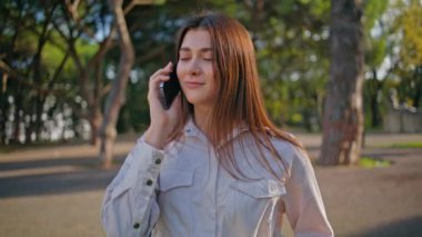 Gülümseyen öğrenci yeşil parkta cep telefonuyla konuşuyor. Mutlu genç bayan akıllı telefon konuşmasını bitir ve güneşli doğada elma ye. Güneşli açık hava ortamında yapılan telefon konuşmalarının neşe kaynağı..