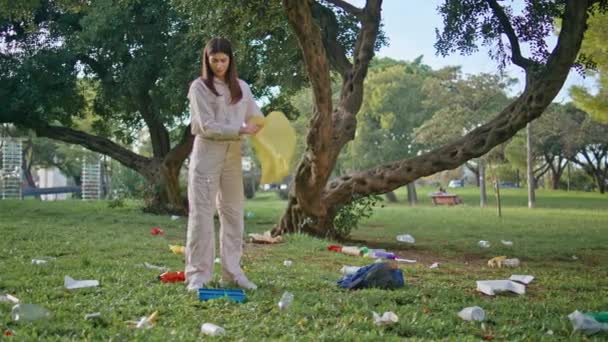 女孩拿着黄色的袋子参加了公园的清理 展示了对环境的管理 生态活跃的妇女为保护自然而收集草皮垃圾 志愿人员清理污染的行动 — 图库视频影像