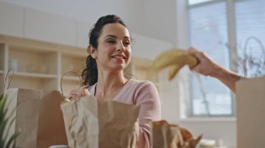 Bir çift mutfakta ürünlerle şakalaşıyor. Komik koca, karısını muzla oynarken güldürüyor. Mutlu gülen eşler birlikte ev mutfağında yiyecek paketleri açıyorlar. Ev idaresi kavramı.