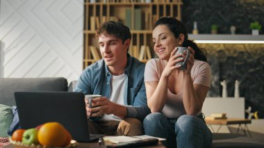 Çift, dizüstü bilgisayarın web kamerasına el sallamayı bitirdi. Keyifli eşler online toplantıda kahve fincanıyla kanepede oturarak vedalaşıyorlar. Sanal internet iletişim konsepti