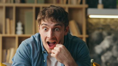 Duygusal adam evde oturma odasında oturarak başarıya seviniyor. Şaşırmış iş adamı, şaşkınlıktan ağzı açık gülüyor zaferden dolayı mutluluk duyuyor. Heyecanlı mutlu adam zaferi kutluyor.