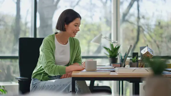 Smiling girl looking laptop screen resting at workplace closeup. Successful young business woman enjoying tasty tea taking break at coworking. Attractive lady holding coffee cup having work pause
