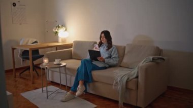 İşyeri sahibi akıllı telefondan gece tabletini arıyor. Akşamları evde bilgisayar kullanan ciddi bir kız. Esmer kadın dijital cihazlı koltukta oturuyor. Odaklanmış Bağımsız İnternet taraması 
