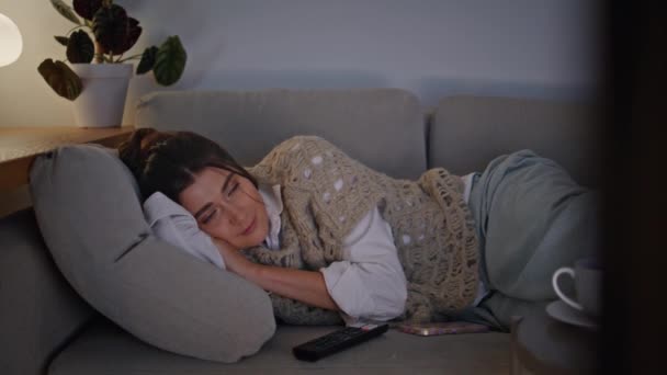 熟睡的女人懒洋洋地躺在沙发上 在晚上的家庭环境中看电视 松松垮垮的女士在舒适的沙发上 在毯子下打盹 家用电器独立睡在灯光灿烂的空气中 — 图库视频影像