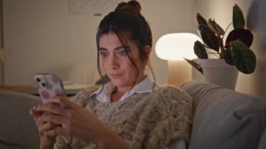 Karanlık Ev 'de akıllı telefondan mesajlaşan odaklanmış bir kız. Sakin, ciddi bir kadın. Akşam oturma odasında cep telefonu sörfü yapıyor. Mutlu kadın koltukta oturmuş cep telefonu ekranına bakıyor. 