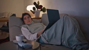 Lamba lambasında duran dizüstü bilgisayarı kullanarak mutlu bir model. Gülümseyen, dingin, yumuşak kanepe istirahati akşam vakti sosyal ağlara tek başına bakan kadın. Sakin esmer kız geceleri ekrana bakıyor.