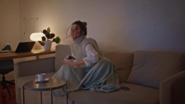 Gülümseyen oyuncu elinde joystickle evde video oyunu oynuyor. Neşeli bir kadın çay fincanı içiyor, oturma odasında dinleniyor. Rahat bir dairede kumanda kullanan heyecanlı bir bayan. Eğlence konsepti