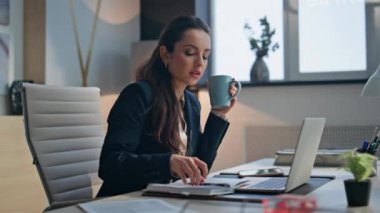 Modern ofis ortamında çayını yudumlayan düşünceli bir iş kadını. Düşünceli profesyonel dinlenme anının tadını çıkarıyor masada sıcak içecek içiyor. Düşünceli resmi kadın notlar yazıyor.