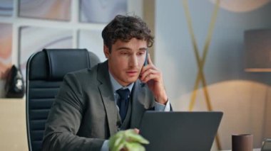 Modern ofiste cep telefonuyla konuşan bir yönetici. Rahatlamış şirket yöneticisi bilgisayardaki kağıtlara bakarak arkadaşça akıllı telefon sohbetinin tadını çıkarıyor. Gülümseyen bir çalışan iş ortağıyla konuşuyor. 