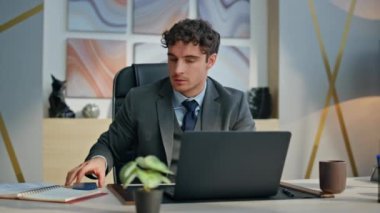 Stresli iş adamı iş yerinde cep telefonuyla bilgisayarı yakın çekimde. Sinirli bir yönetici iş yerinde başarısız olduğu için sinirli hissediyor. Sinirli adam cep telefonu okuyup duygusal hareketler yapıyor.