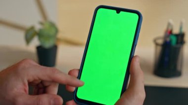 Öğrenci parmağı kromakey cep telefonu görüntüleme sitesinde internet taraması yapıyor. Bilinmeyen adam modern akıllı telefon kullanıyor. Kapalı mekanda ekran motifi var. İş yerinde yeşilekran kaydırma aygıtı