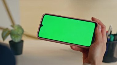 İş kadını elinin altında cep telefonu var. Çalışma masasında oturuyor. Modern ofiste yeşil ekran akıllı telefonu izleyen kimliği belirsiz bir kadın. Yönetici eğitici görünümlü çevrimiçi webinar kromakey hücre